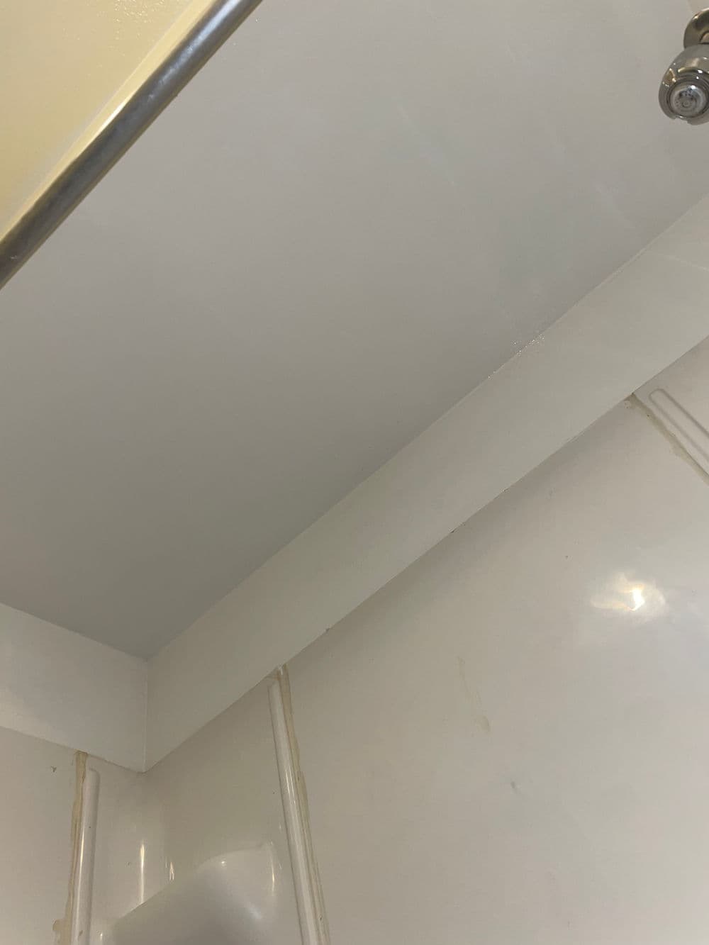 Ceiling of a shower with light reflections and white tiled walls.